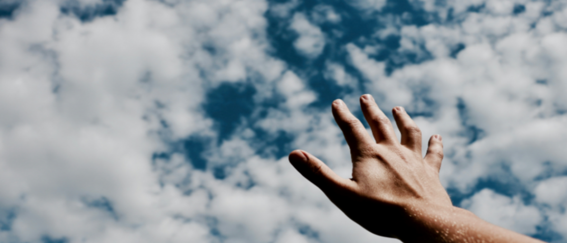 Hand reaching to clouds in the sky