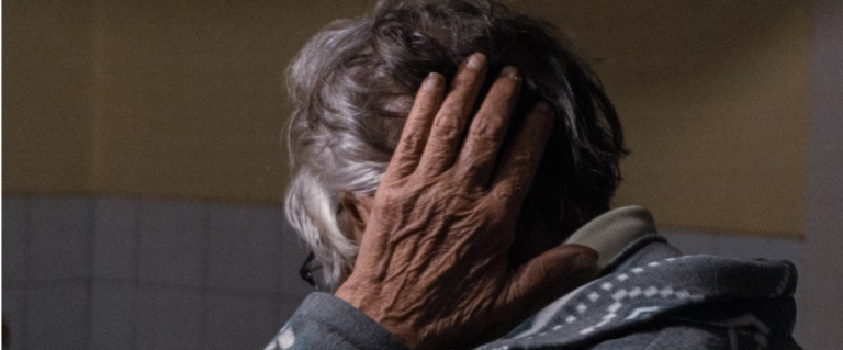 older woman, wearing a fleecy cardigan, covering her ear