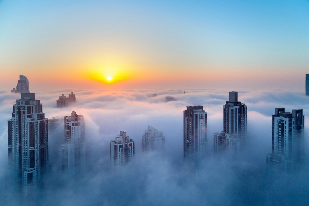 Picture of a horizon with the sun setting. Taken from the vantage point above skyscrapers emerging from heavy fog. 