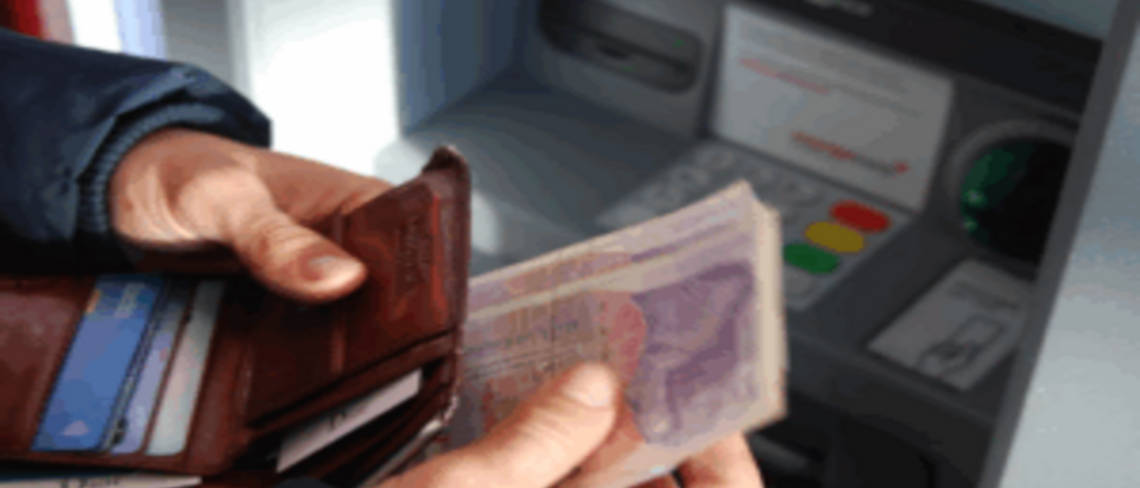 Hands putting money into a wallet in front of a cash machine