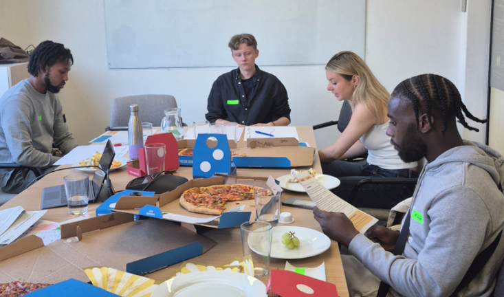 A photograph four young people sat around a desk eating and discussing as a group, taken as part of this project's participatory workshops